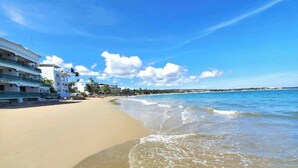 Ein Strandhotel mit mehreren Etagen und Balkonen, ein Sandstrand und strahlend blauer Himmel.