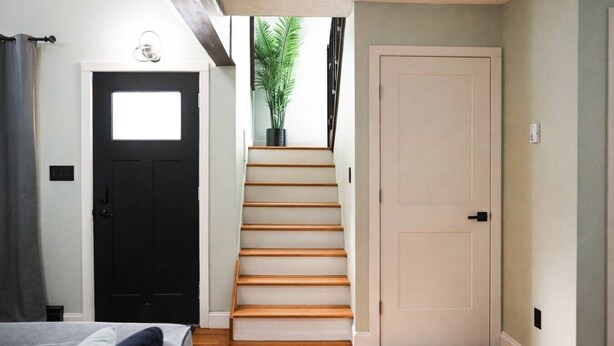 Eine Treppe führt zu einer Tür, ein Bett mit einem Kopfkissen und eine Pflanze in der Ecke.