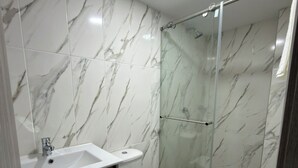 A bathroom with a marble wall, a sink, a toilet, and a glass shower enclosure.