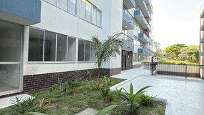 A modern multi-story building with balconies, a landscaped garden with various plants, and a paved walkway.