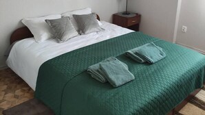 A neatly made bed with a green quilt, two pillows, and folded towels on a wooden floor. - Kielce Urban Oasis Apartment (Kielce)