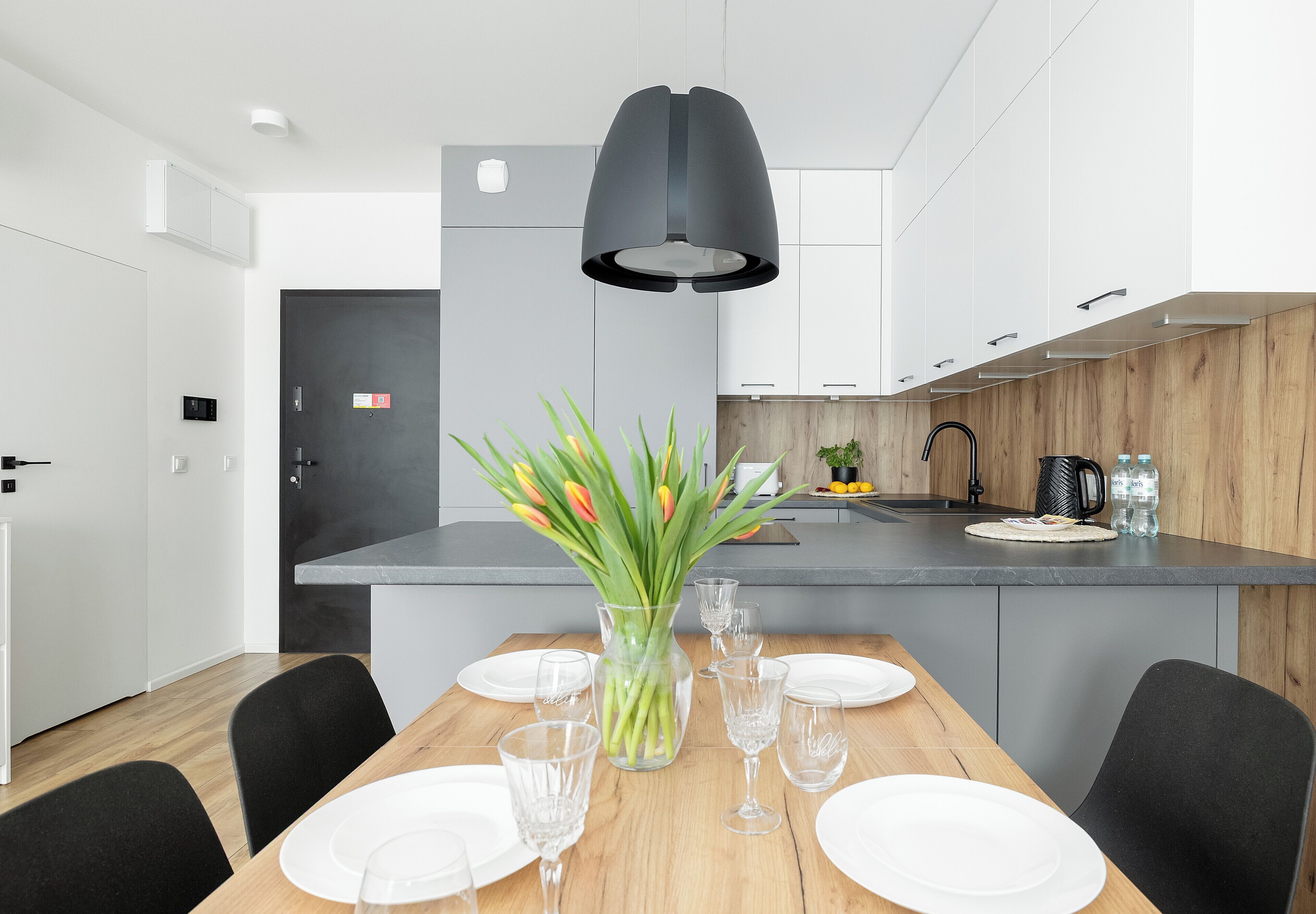 Une cuisine moderne avec des meubles blancs, un plan de travail en bois et un luminaire suspendu noir.
