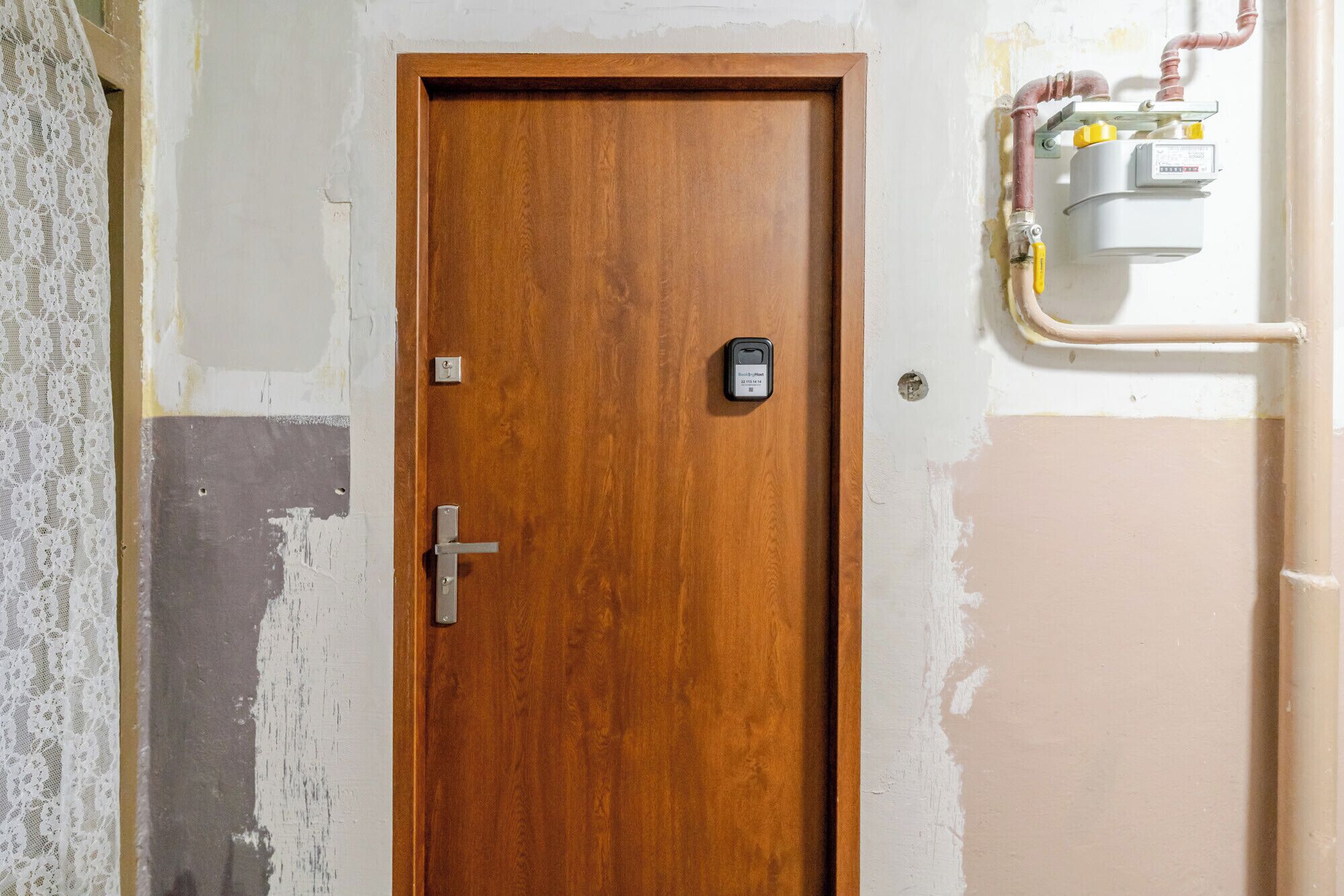 Een houten deur met een slot en sleutelgat, een elektrisch verdeeldoos bevestigd aan de muur, en blootliggende bedrading.