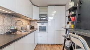 Una cocina compacta con armarios blancos, microondas, lavamanos y piso de madera.
