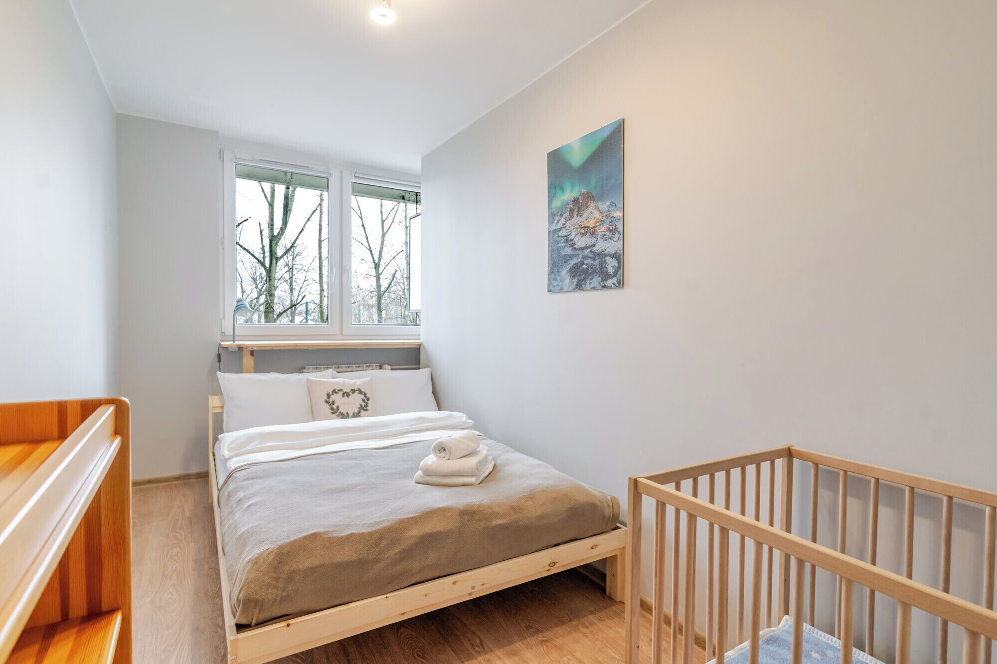 Een slaapkamer met een bed, een ledikant, een raam met uitzicht op bomen, en een schilderij aan de muur.