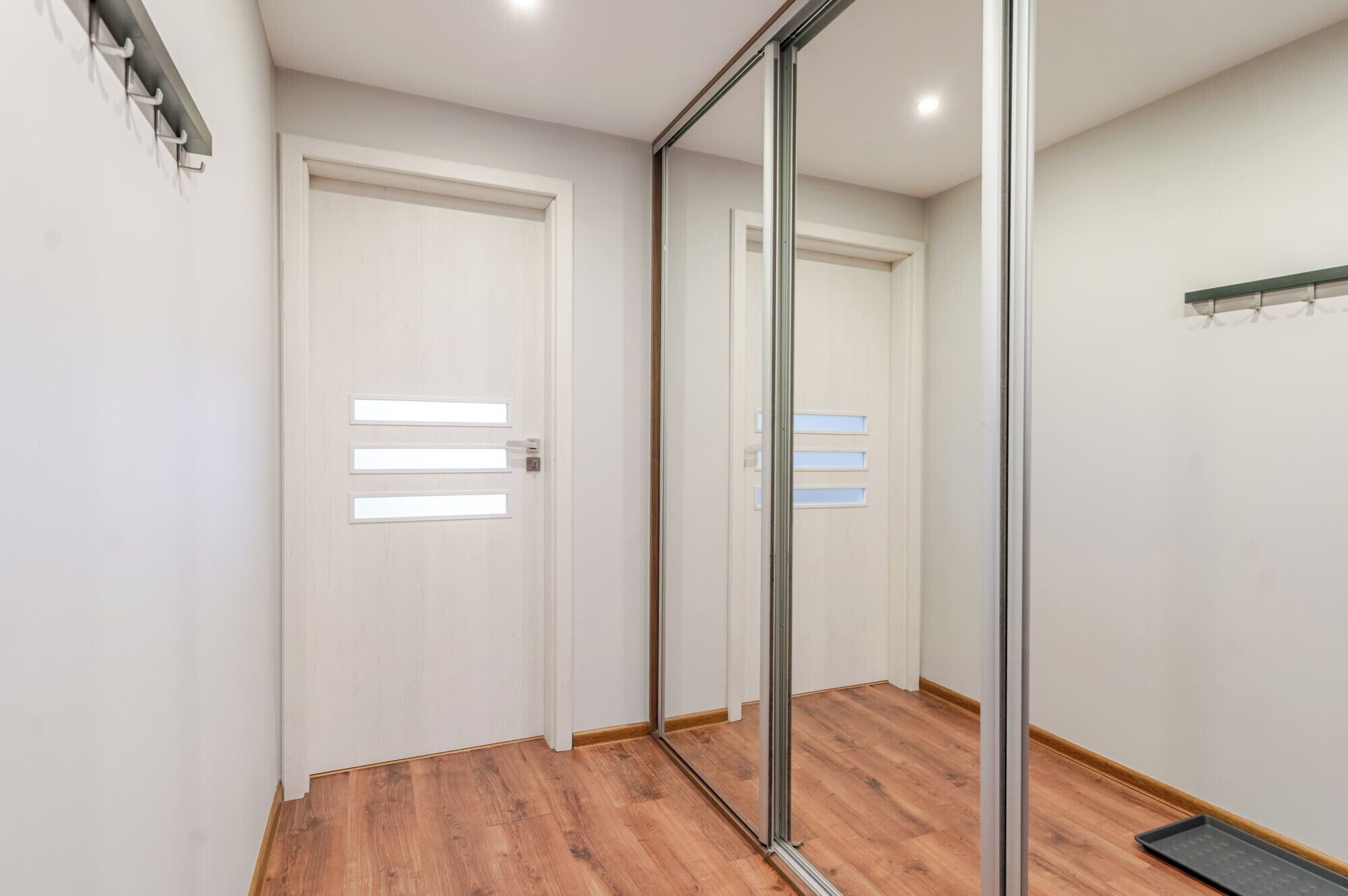Un couloir doté d’un plancher en bois, de portes blanches avec des panneaux en verre dépoli et d’un miroir à cadre métallique sur le mur de droite.