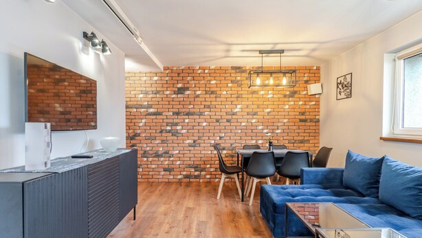 Una sala de estar moderna con pared de ladrillo, un sofá, una mesa de centro y un comedor con sillas y una mesa.