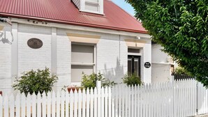 Un bâtiment blanc avec un toit rouge, une clôture blanche en bois et une plaque indiquant qu’il s’agit de Hurst Cottage.