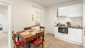 Une cuisine compacte avec des meubles blancs, une table à manger en bois et des chaises rouges, ainsi qu’une fenêtre laissant entrer la lumière naturelle.