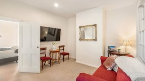 Une chambre d’hôtel avec un lit, un canapé rouge, une télévision, une petite table avec des chaises et un miroir.
