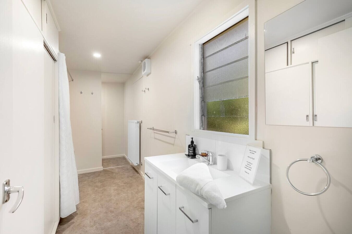 A narrow bathroom with a white sink, a towel rack, and a window with a metal screen.