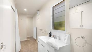 A narrow bathroom with a white sink, a towel rack, and a window with a metal screen.