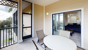 A balcony with a table and chairs, a sliding glass door leading to a living area with a couch and a coffee table. - 3rd floor condo w/ pools, balcony, sauna, gym, hot tub, near theme parks (Kissimmee)
