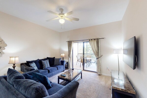 A living room with a sofa set, a coffee table, a ceiling fan, and a TV mounted on the wall. - 3rd floor condo w/ pools, balcony, sauna, gym, hot tub, near theme parks (Kissimmee)