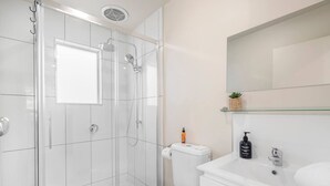 A modern bathroom with a glass-enclosed shower, a toilet, and a sink with a mirror above. - Private North Hobart Cottage (North Hobart)