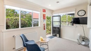 A room with a radiator, a blue chair, a small table with candles, a black door, a clock, and a TV mounted on the wall. - Private North Hobart Cottage (North Hobart)