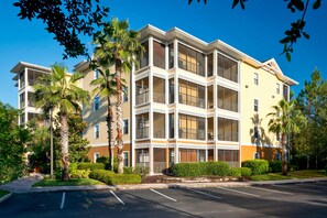 A multi-story hotel with balconies, a parking lot, and palm trees. - 4th floor condo w/ shared pools, hot tub, gym, balcony, sauna, near theme parks (Kissimmee)