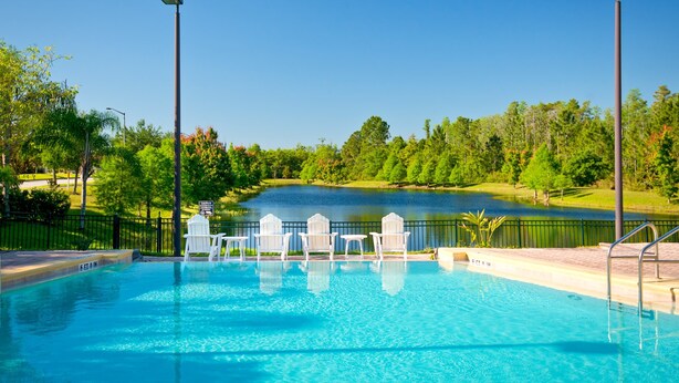 Una piscina con sillas blancas y vistas a un lago y árboles.
