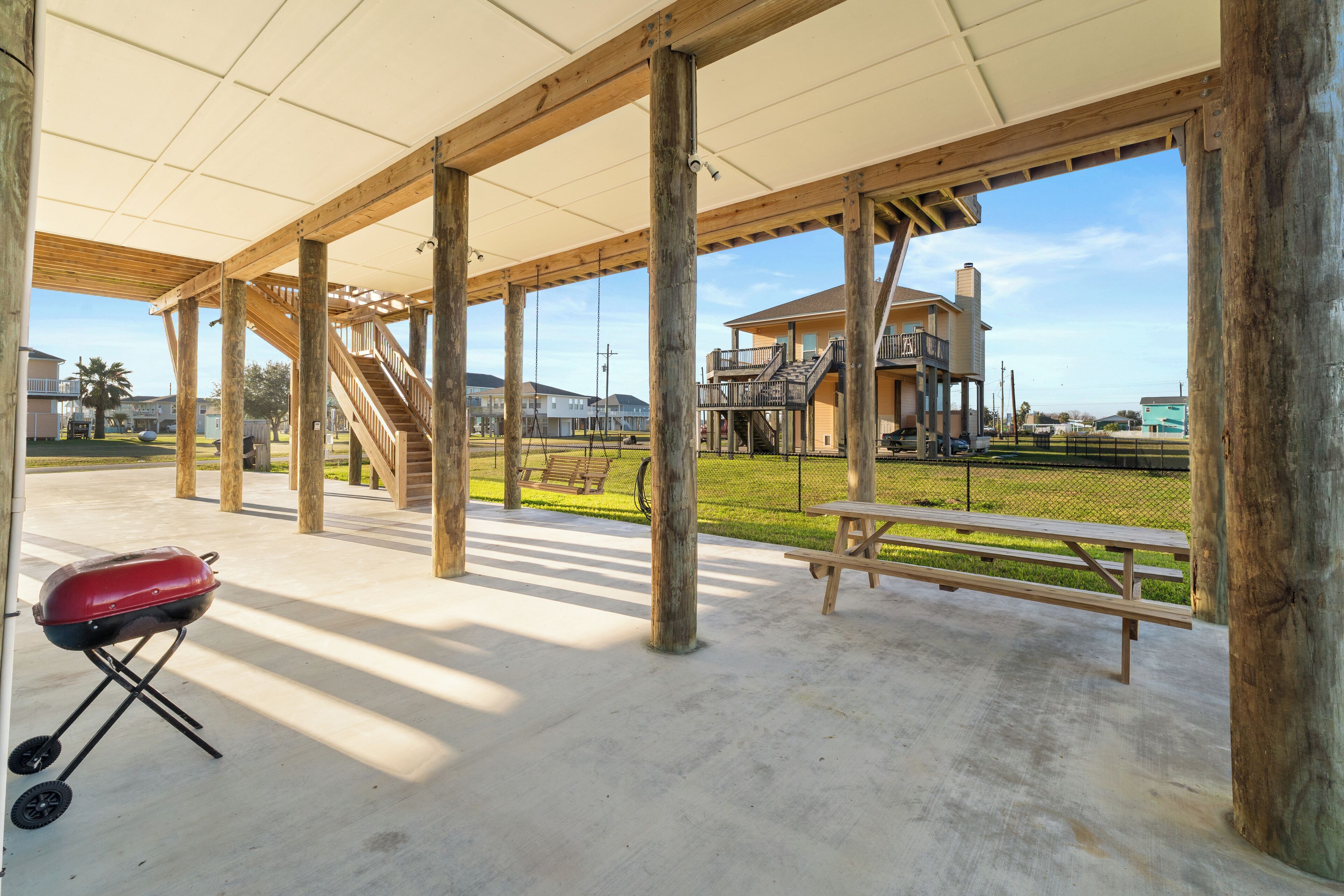 Un espacio al aire libre con techo, que cuenta con una parrilla, mesas de picnic y vistas a un edificio residencial.