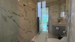Une salle de bain moderne dotée d’une douche à parois de verre, de murs en marbre et offrant une vue dégagée sur l’extérieur.