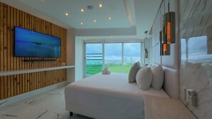 Ein modernes Schlafzimmer mit einem großen Bett, einem Fernseher an der Wand und Blick auf die Stadt durch die Fenster.