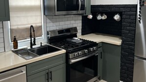 Una cocina moderna con estufa, horno y microondas de acero inoxidable. Hay un lavamanos con grifo, y los armarios son de color verde oscuro.