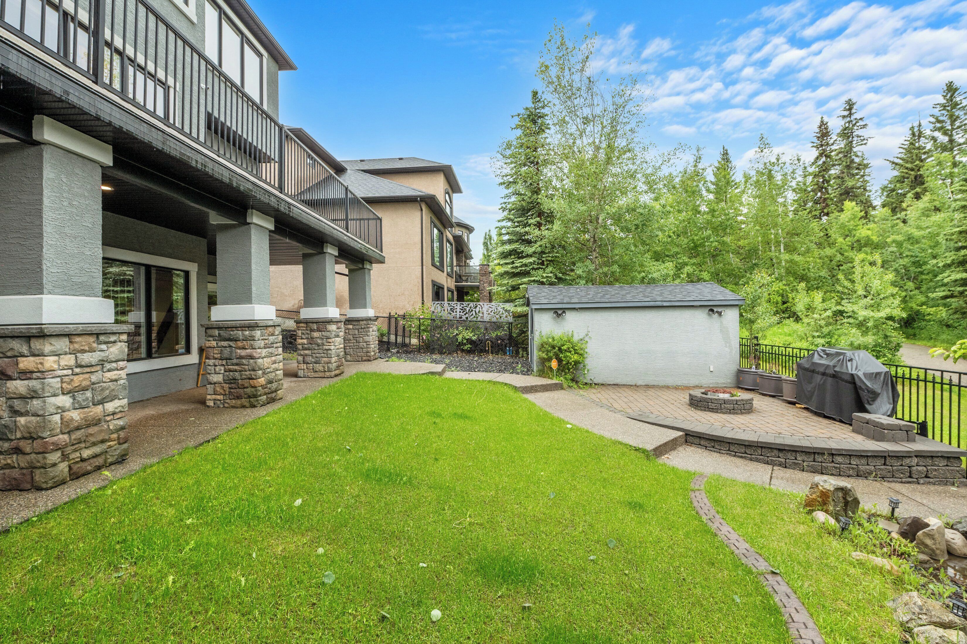A residential property with a well-maintained lawn, stone pillars, a small shed, and a barbecue area.