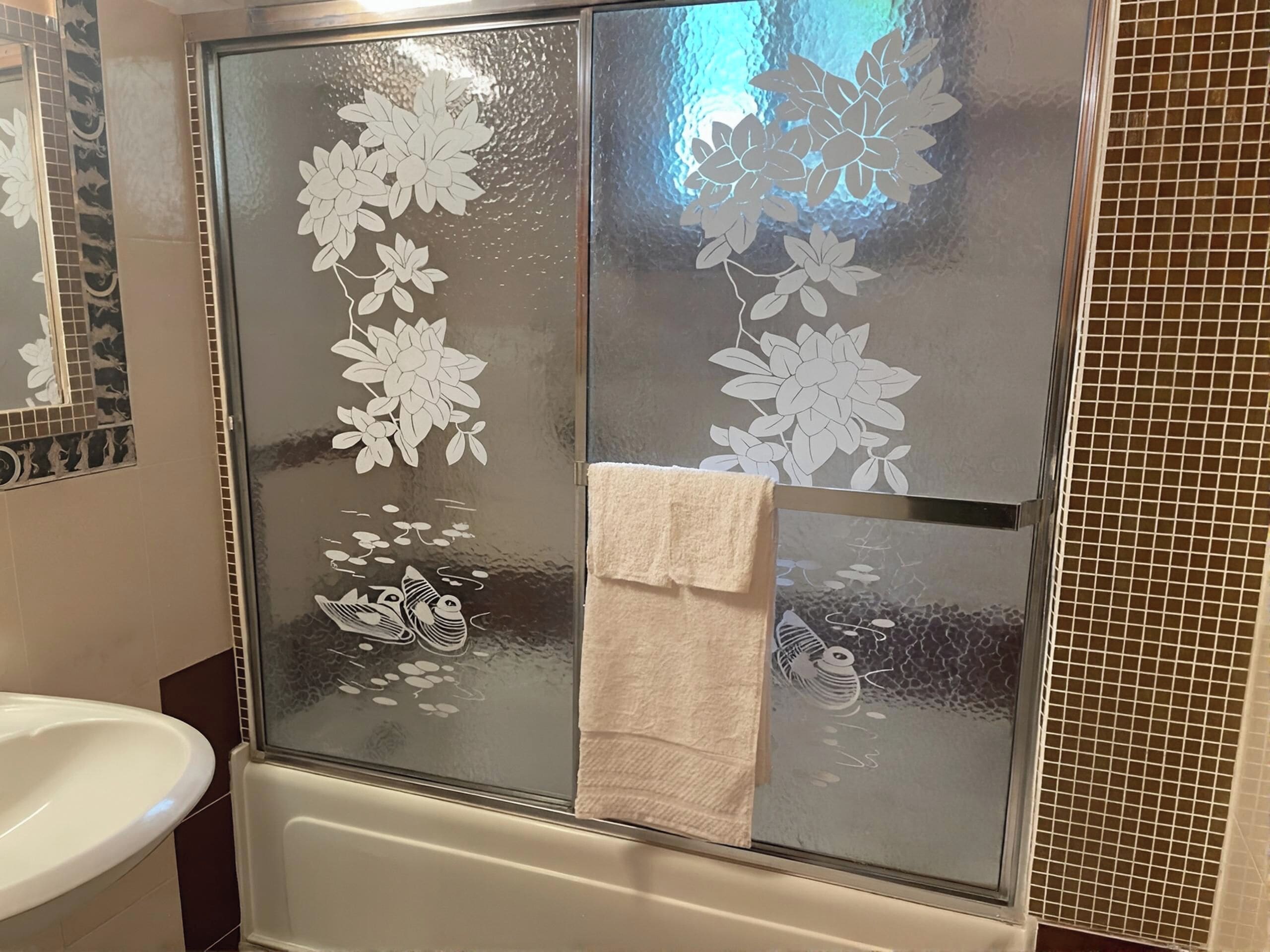 Bany amb box de dutxa de vidre, un lavabo blanc i un suport per tovalloles.
