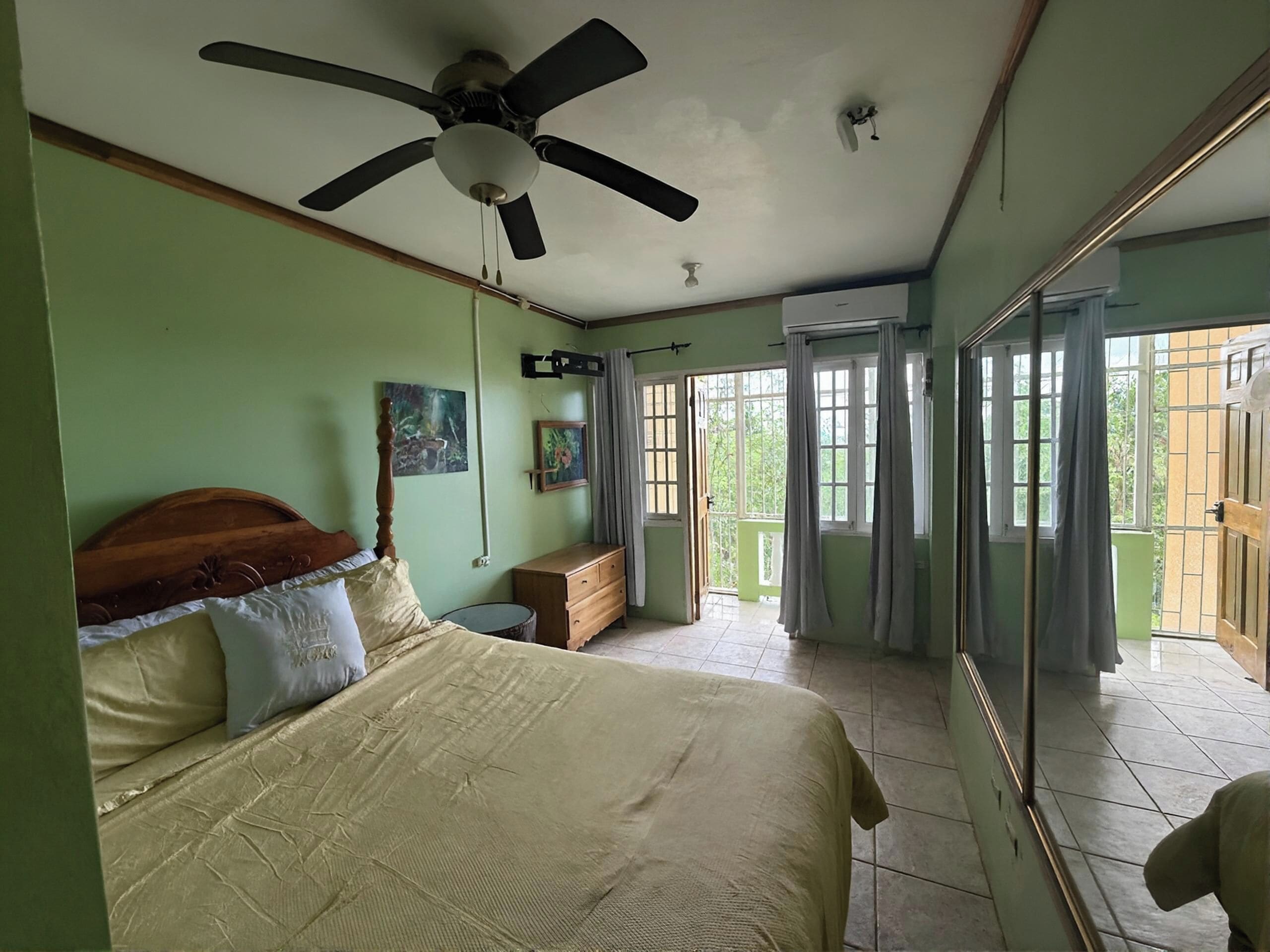 Un dormitorio con cama, ventilador de techo, cómoda y puerta corrediza de vidrio que da a un balcón.