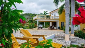 Un bâtiment jaune doté d’un patio couvert, d’un espace extérieur aménagé avec des sièges et d’un chemin en pierre.
