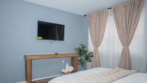Una camera da letto con un letto, un comodino, una TV a muro e una finestra con tende.
