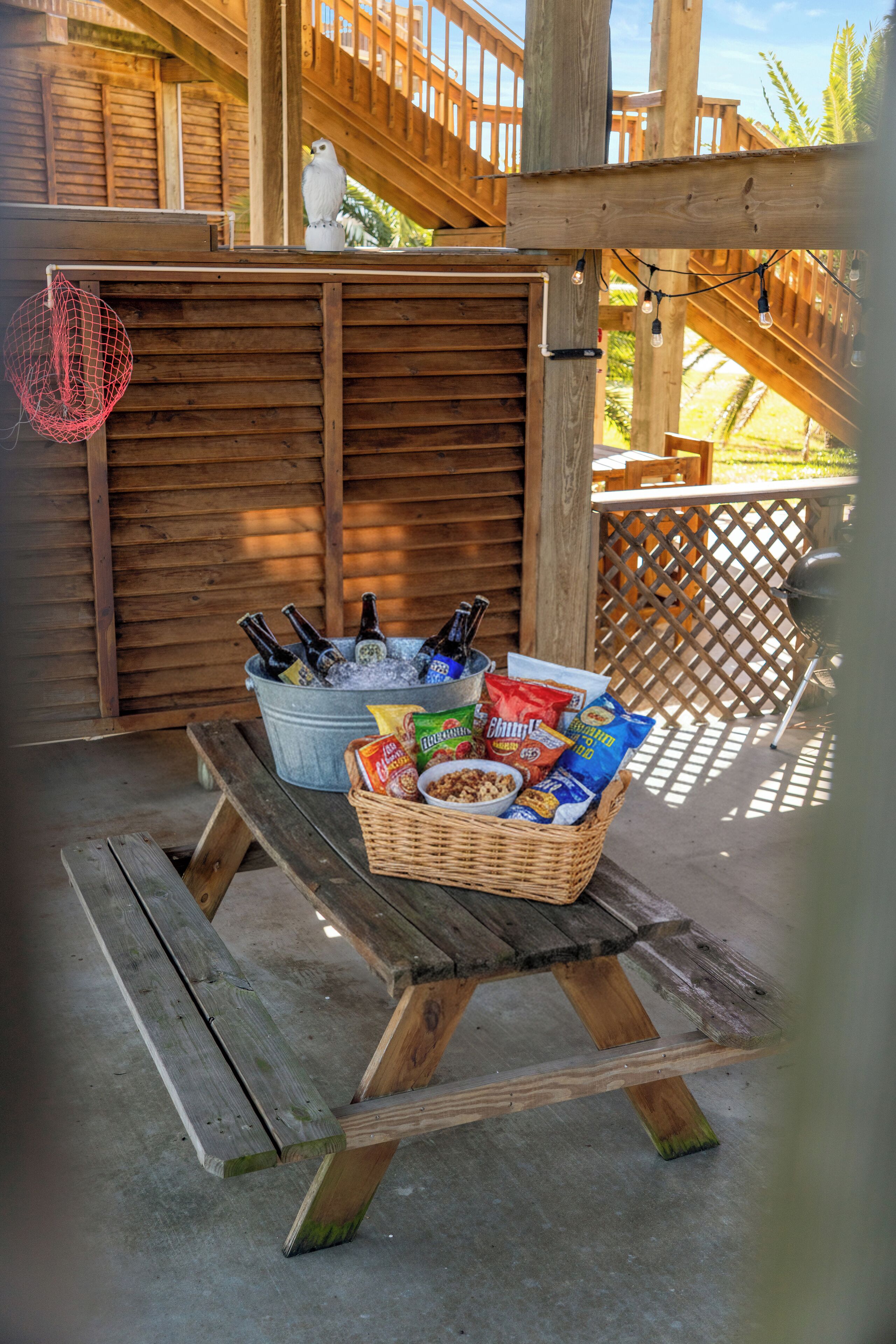 A wooden deck with a picnic table holding a basket of snacks, bottles, and a bird feeder.