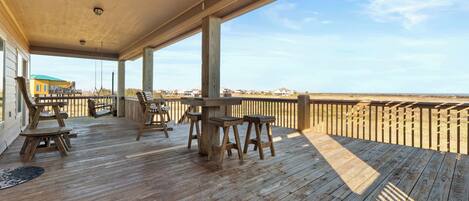 A wooden deck with outdoor furniture, a view of the beach, and a clear sky.