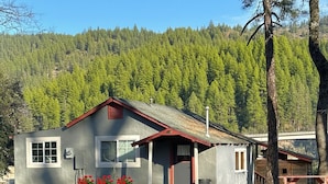 Ein kleines, einstöckiges Gebäude mit rotem Dach und grauen Wänden, gelegen in einer bewaldeten Gegend mit freiem Blick auf einen Berg im Hintergrund.