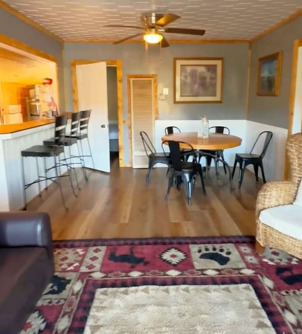 A dining area with a round table, chairs, a ceiling fan, and a kitchen area with a counter and chairs. - Lakeshore Resort (Lakehead)
