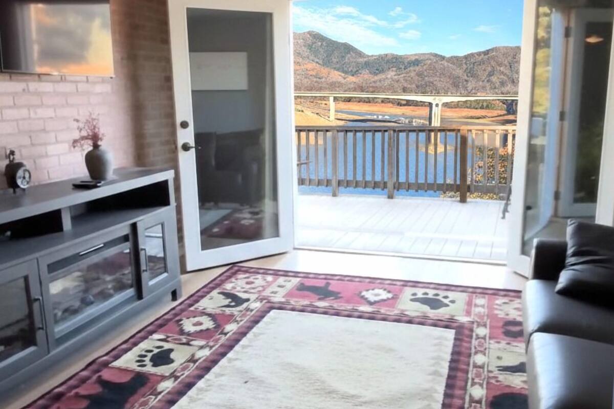 Une pièce dotée d’un ventilateur de plafond, d’un téléviseur fixé au mur et d’une porte-fenêtre coulissante donnant sur un balcon avec vue sur la montagne.