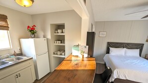 Eine kleine Küche mit Holztisch, Kühlschrank und Bett mit Holz Kopfteil.