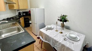Cocina compacta con fregadero, estufa y refrigerador. Una mesa de comedor con mantel blanco y un jarrón de flores.