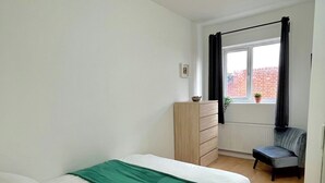 Un dormitorio con cama, cómoda, silla y ventana con cortinas.