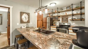 A kitchen with granite countertops, stainless steel appliances, and a wooden bar stool area.