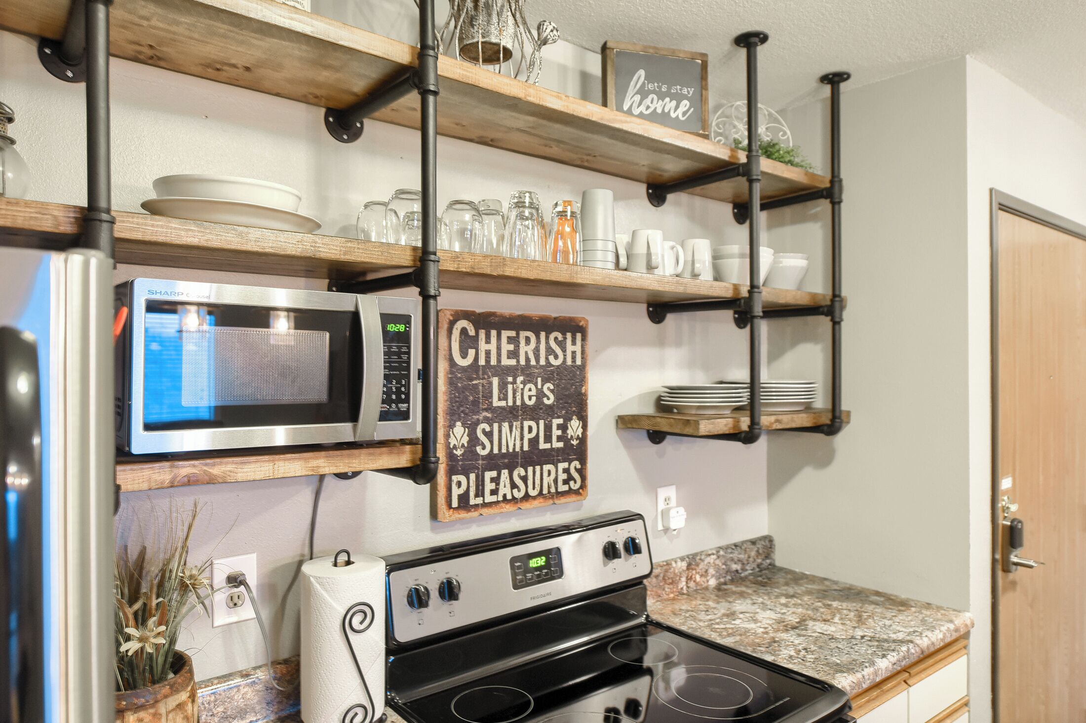 A kitchen with a stainless steel microwave, a stove, and shelves above holding dishes and jars.