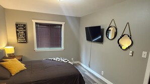 A bedroom with a bed, a window with blinds, a TV, and wall-mounted mirrors.
