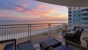 A balcony with wicker furniture, a view of the ocean, and a building with balconies. - Amazing Gulf Views! Legacy Towers 10th Floor! (Gulfport)