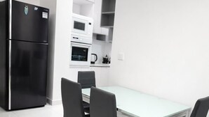 A modern kitchen with a black refrigerator, white cabinets, a microwave, and a coffee maker. There is a glass-top table with four chairs.