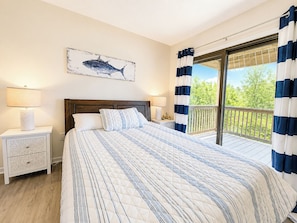 A bedroom with a large bed, two bedside tables, a nightstand, a window with curtains, and a view of greenery outside. - Our Haven - 5 BR Soundside Vacation Home in Duck w/Private Pool, Dogs Allowed (Duck)