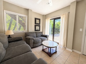 A living room with a sofa, a round table, and a window with blinds. - Our Haven - 5 BR Soundside Vacation Home in Duck w/Private Pool, Dogs Allowed (Duck)