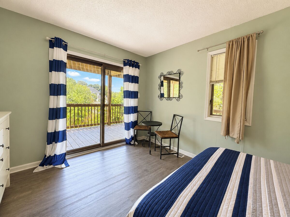 Un dormitorio con cama, una silla, una mesa, un ventanal y un balcón.