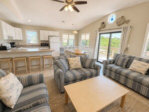 A spacious living room with striped sofas, a wooden coffee table, and a kitchen area in the background. - Our Haven - 5 BR Soundside Vacation Home in Duck w/Private Pool, Dogs Allowed (Duck)