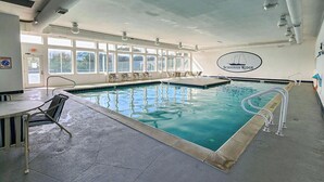 An indoor swimming pool with clear water, a lifeguard chair, and a logo on the wall. - Daisy Duck - 5 BR Semi-Oceanfront Home in Schooner Ridge, Duck (Duck)