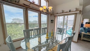 A dining area with a glass table and chairs, large windows, and a chandelier. - Daisy Duck - 5 BR Semi-Oceanfront Home in Schooner Ridge, Duck (Duck)